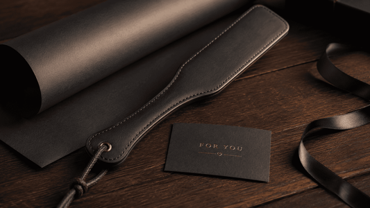 leather paddle beside simple dark gift wrapping and card on wooden surface