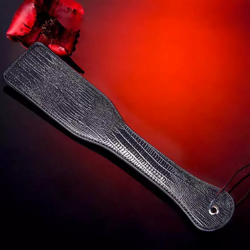 Black textured spanking paddle displayed against red atmospheric background
