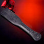 Black textured spanking paddle displayed against red atmospheric background