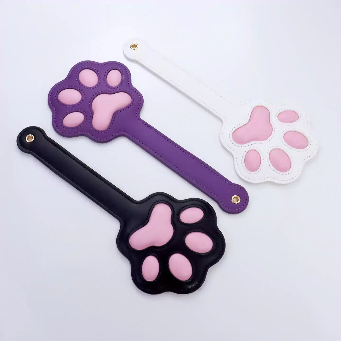 Black, white and purple cat paw silicone spanking paddles displayed together