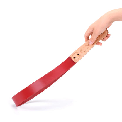 Red leather BDSM paddle with carved wood handle on white background